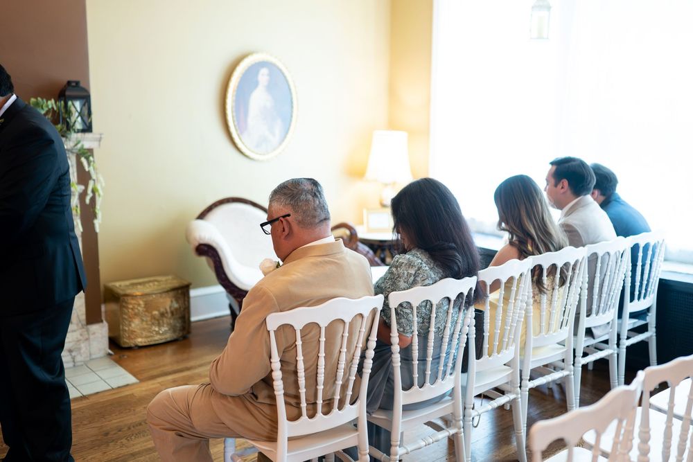 Guests seated in white chairs during an intimate indoor wedding ceremony in an elegantly decorated room.