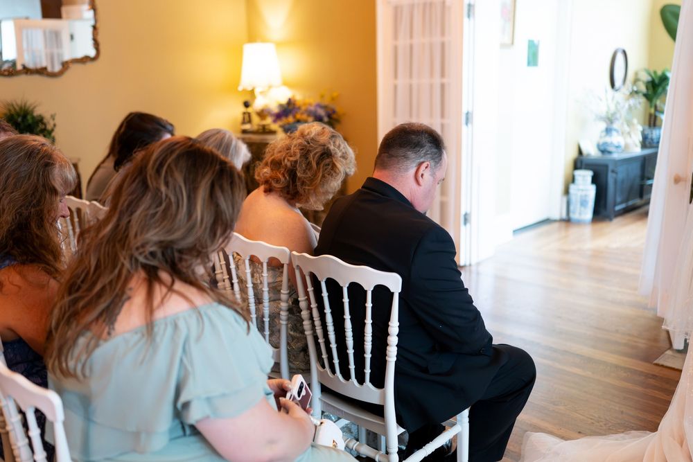Wedding guests seated in white chairs during an intimate indoor ceremony in a warmly lit venue.