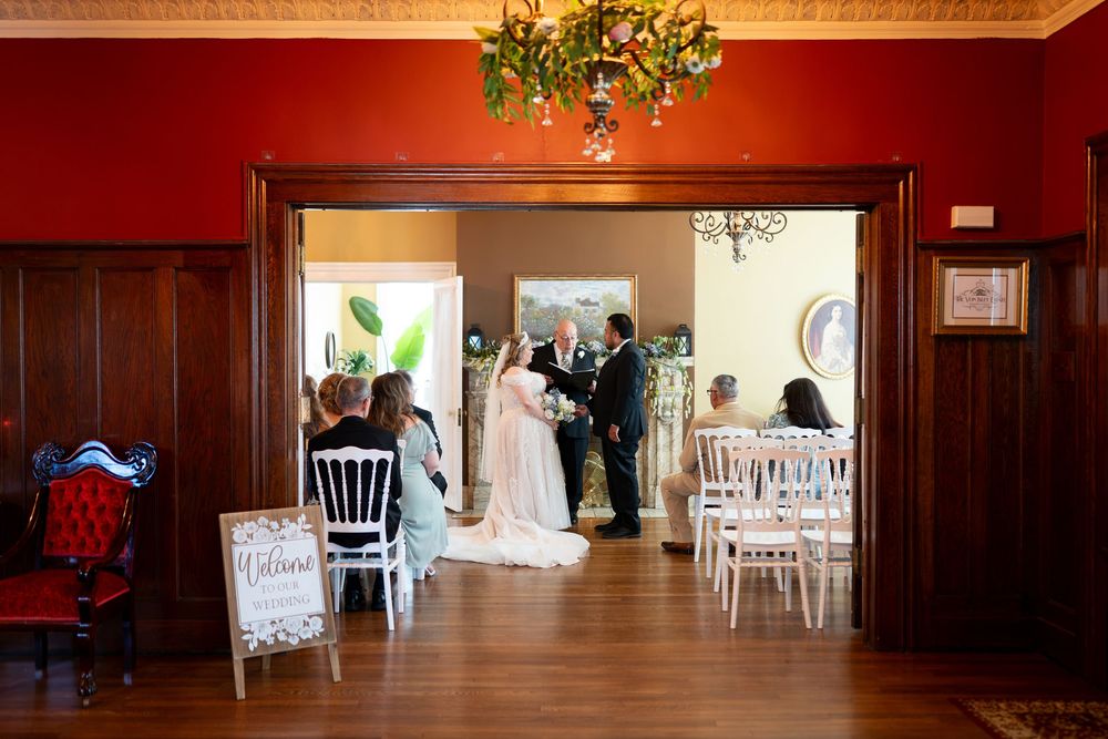 Elegant wedding ceremony in a red-walled venue with bride, groom, and officiant framed in a doorway.
