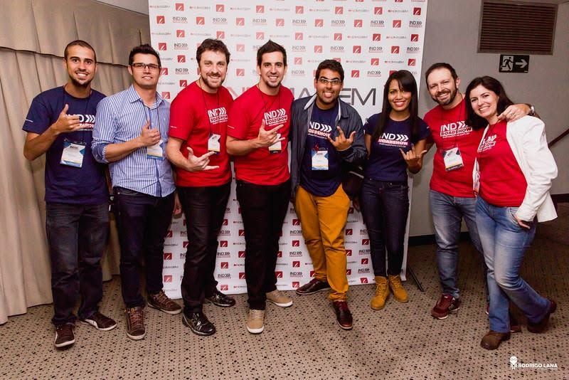 Group of eight smiling professionals posing together at a corporate event, wearing red and navy branded t-shirts.