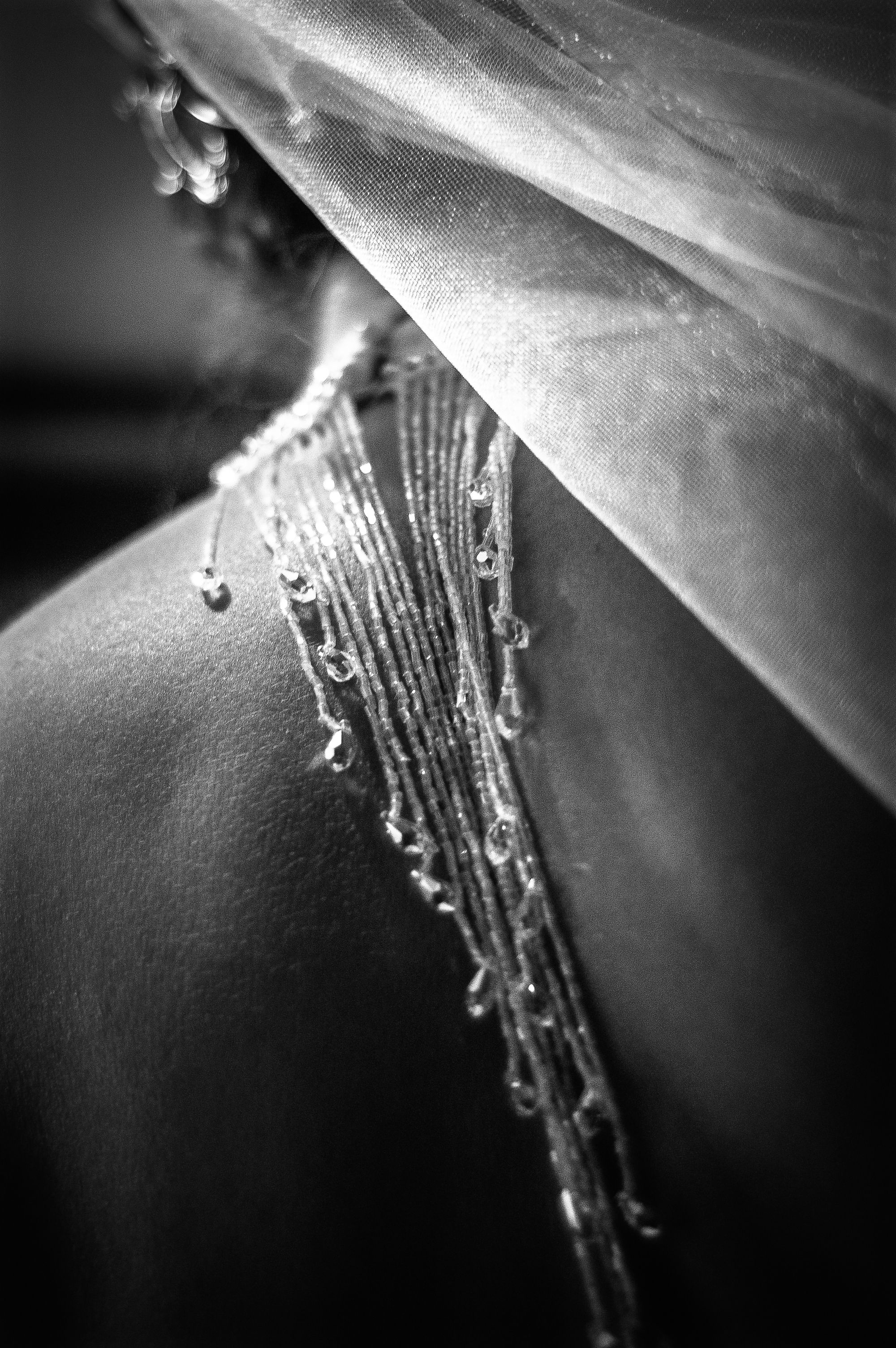 Close-up black and white detail of a wedding dress back with delicate beaded straps and sheer veil.