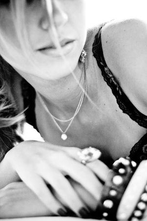 Black and white close-up of a woman wearing layered pearl necklaces, a lace top, and statement rings.