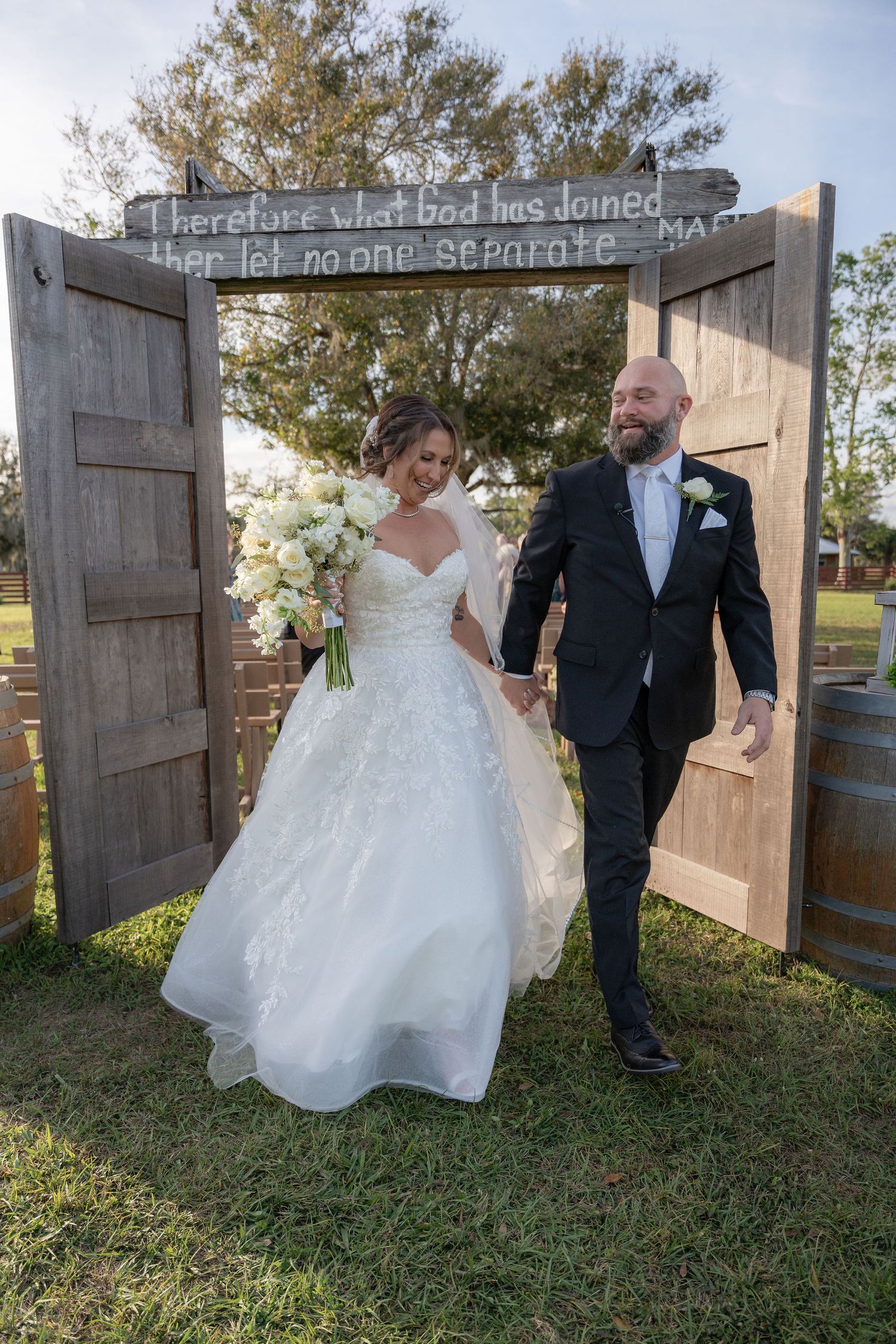 Newlyweds walking back down the aisle through the wooden barn door arch at a Rockin' H Ranch wedding in Palm City, FL
