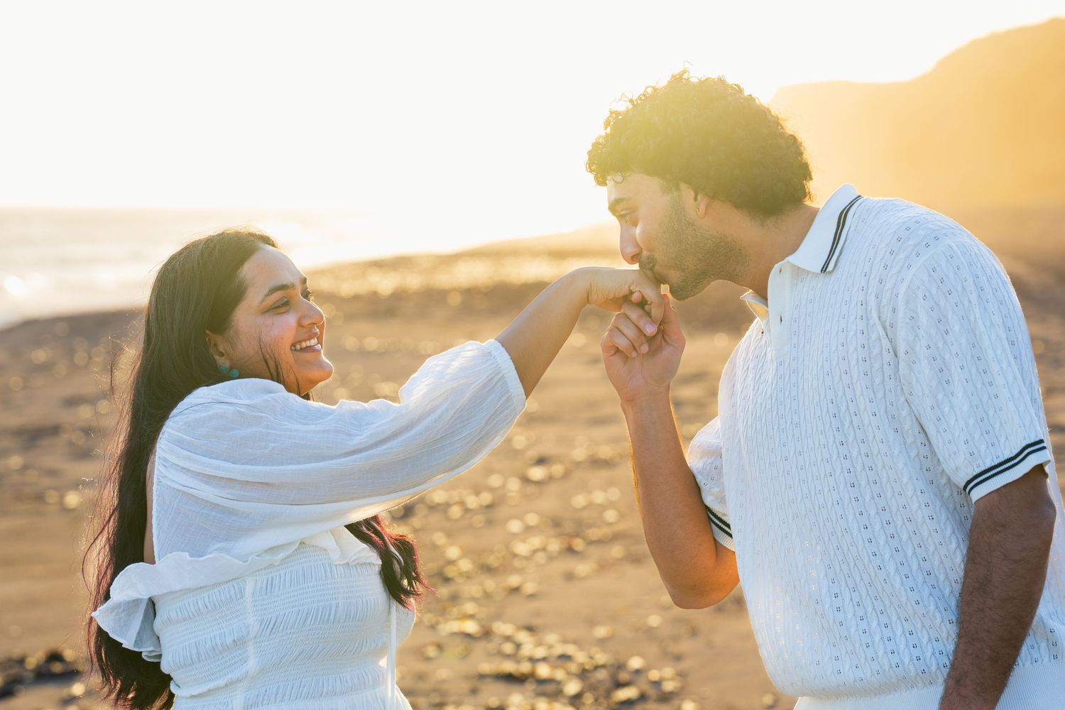 A couple photo of a man kissing the woman's hand while on the beach during sunset. A couple portrait taken in LA county