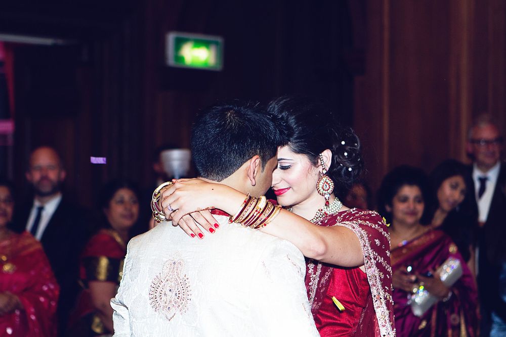 Couple sharing first dance at Indian wedding reception, bride in red sari with mehndi, groom in white sherwani.