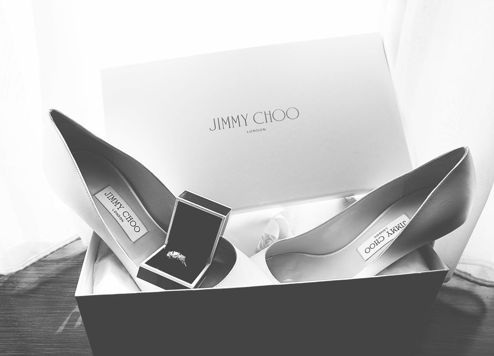 Black and white photo of Jimmy Choo heels in box with a diamond ring, elegant bridal accessories.