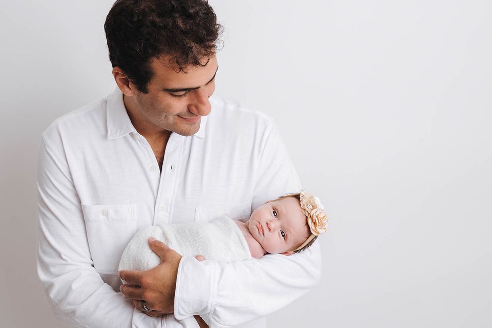Man in white shirt tenderly holding a newborn baby against a white background.