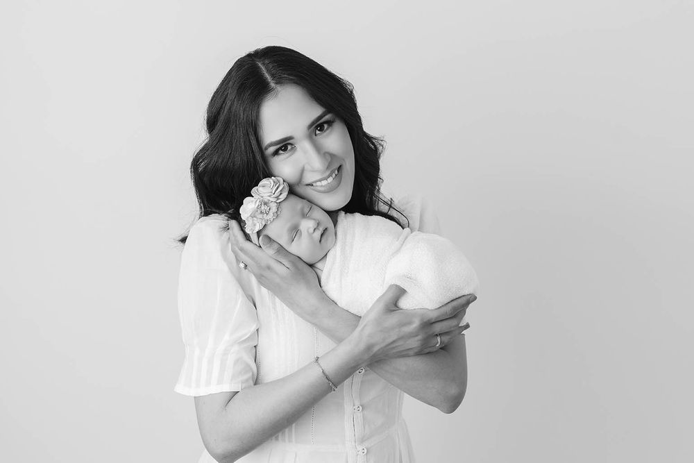 Black and white photo of a smiling young woman holding a sleeping newborn baby close to her cheek.
