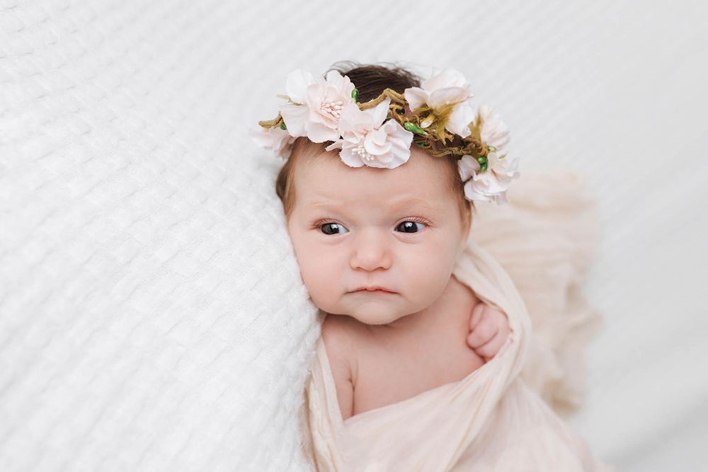 Newborn baby girl wearing a delicate floral crown wrapped in soft cream fabric.