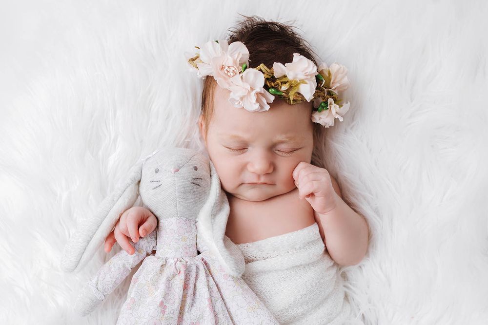 Sleeping newborn baby girl with pink floral crown cuddling a bunny stuffed animal.