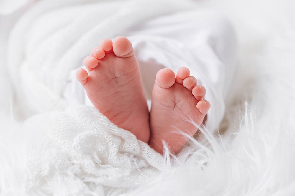 Close-up of tiny newborn baby feet wrapped in soft white fabric.