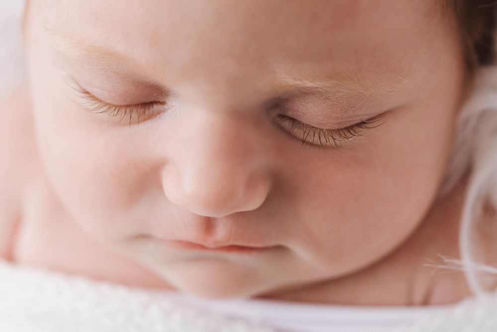 Extreme close-up of sleeping newborn baby face showing delicate eyelashes and soft skin details.