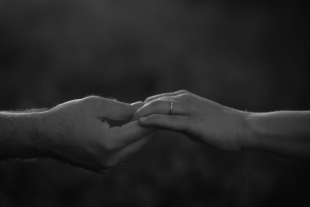 Black and white close-up of two hands touching fingertips with an engagement ring visible.