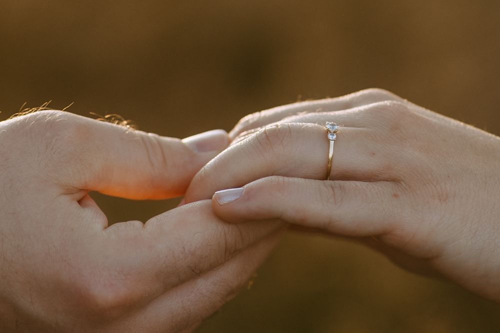 Close-up of hands placing a diamond engagement ring on a finger during a proposal.