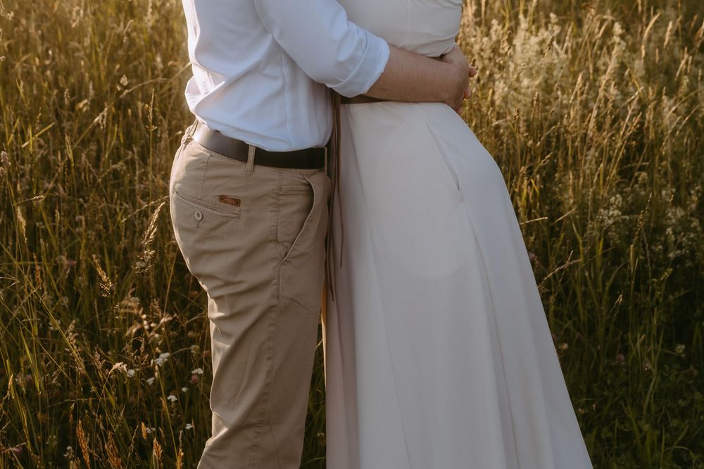 Couple embracing in golden field, woman in white wedding dress, man in khaki pants and white shirt.