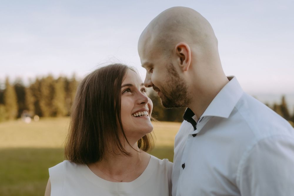 Smiling couple gazing at each other outdoors with trees and field in background during golden hour.