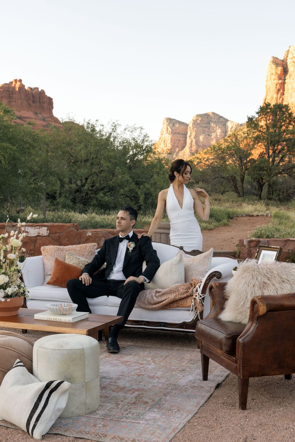 Couple in wedding attire seated on white sofa with desert red rock canyon backdrop in Sedona Arizona.