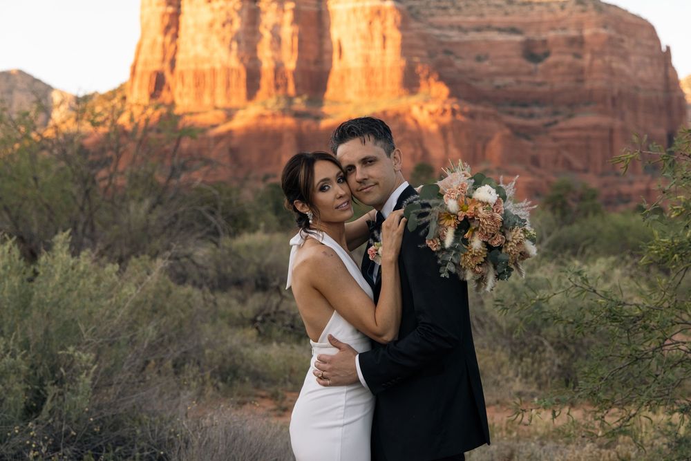 Couple embraces at golden hour in Sedona, Arizona, with red rock formations and desert landscape backdrop.
