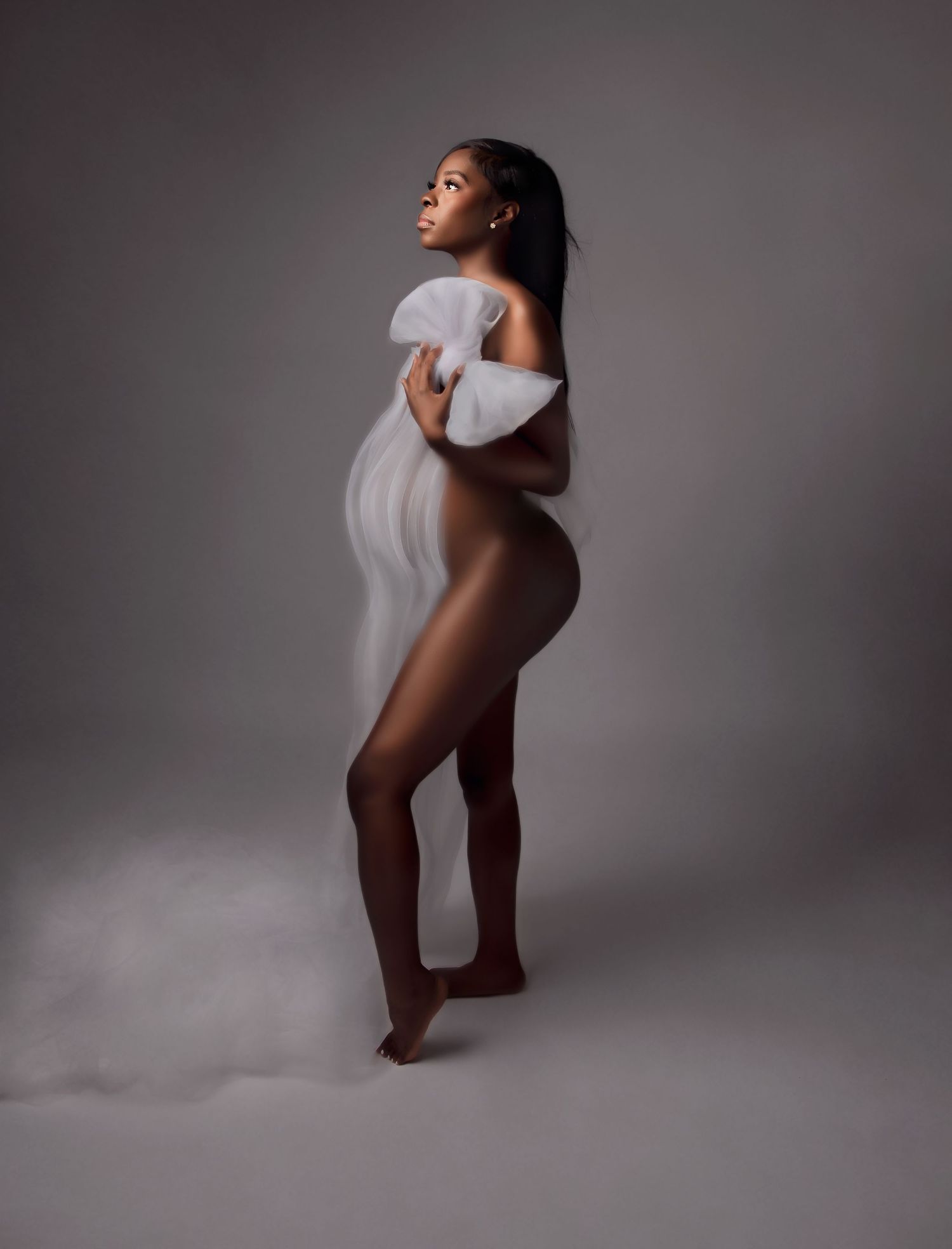 Pregnant woman posing elegantly with flowing white fabric in a professional studio maternity photography session.