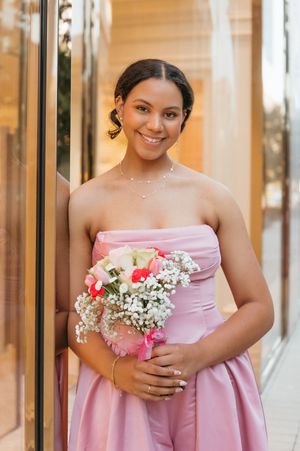 Young woman in strapless pink gown holding bouquet of white and pink flowers.