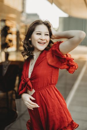 Young woman in red ruffled dress smiling outdoors in urban setting.