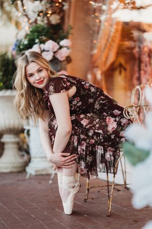 Blonde woman in floral dress posing in ballet pointe shoes near flowers.