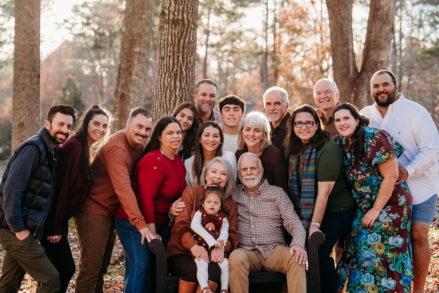 A large multigenerational family poses together in an autumn forest.