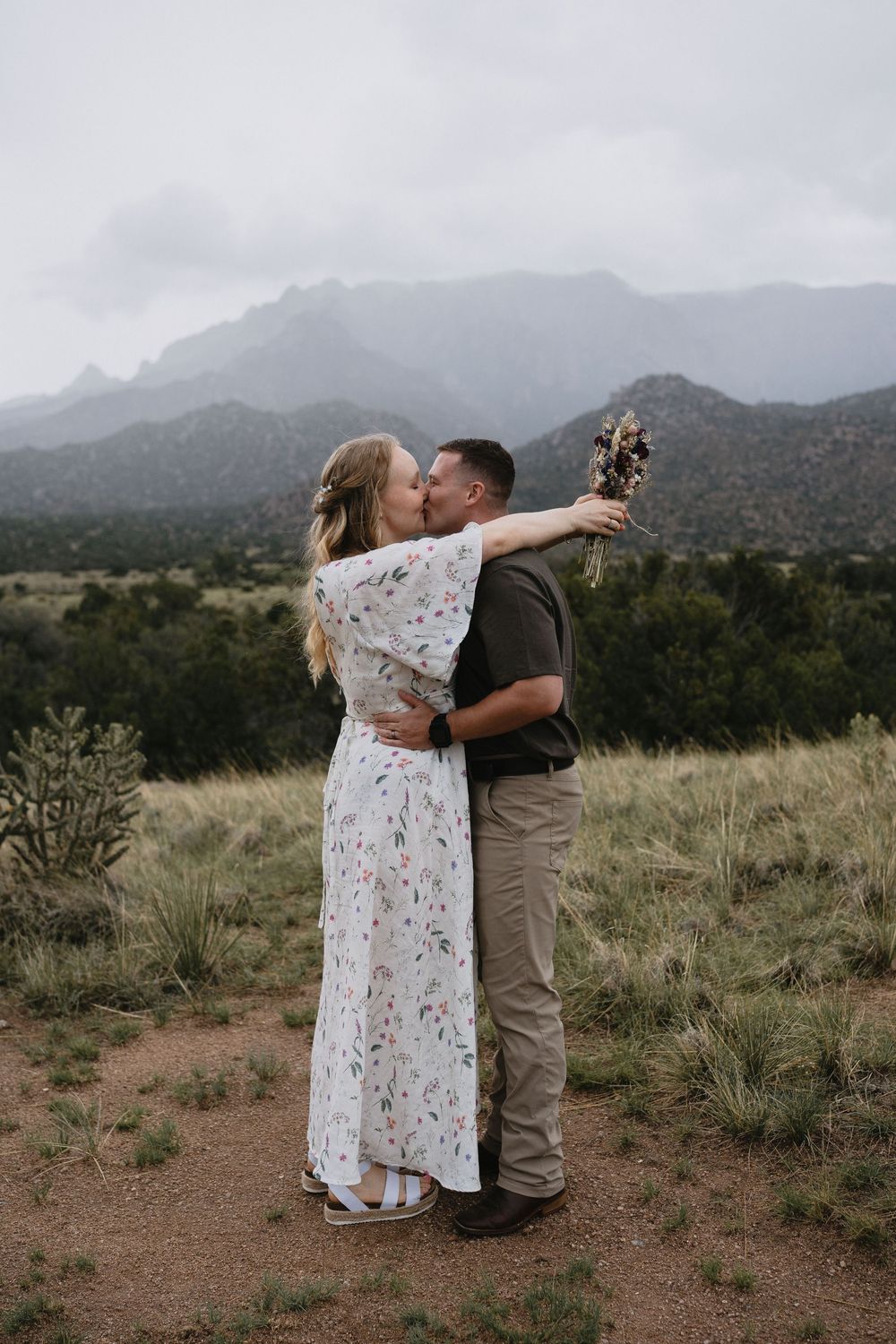 Newlyweds share a kiss in a scenic desert landscape with mountains in the background in Elena Gallegos Trailhead