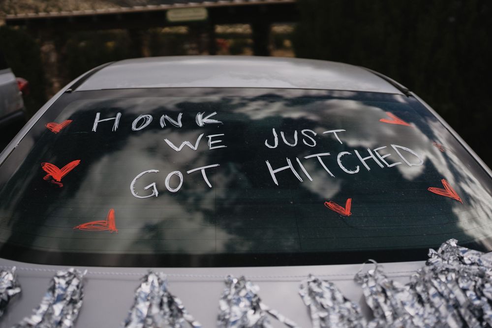Car rear window decorated with Honk We Just Got Hitched wedding message and red hearts.