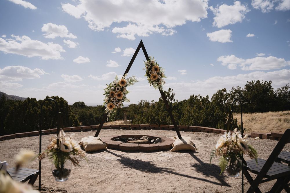 Triangular wedding arch decorated with sunflowers and white blooms over a stone fire pit.