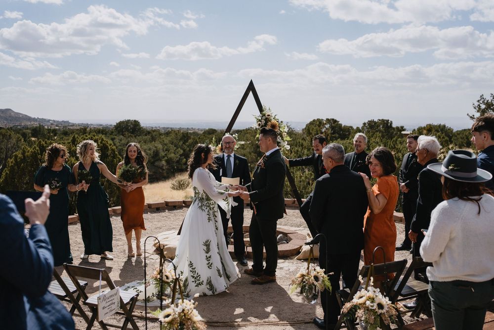 Bride and groom exchange vows at outdoor wedding ceremony with triangular arch and desert landscape backdrop at Elena Gallegos Trailhead