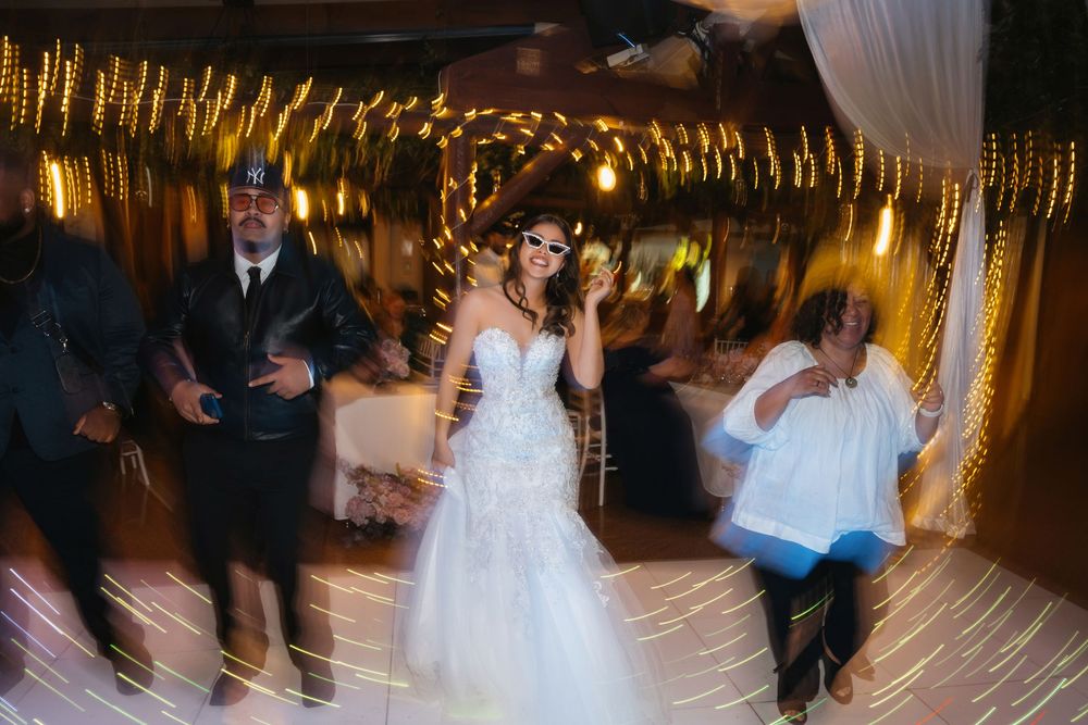 Bride in white mermaid gown dancing joyfully with guests at a warmly lit wedding reception.