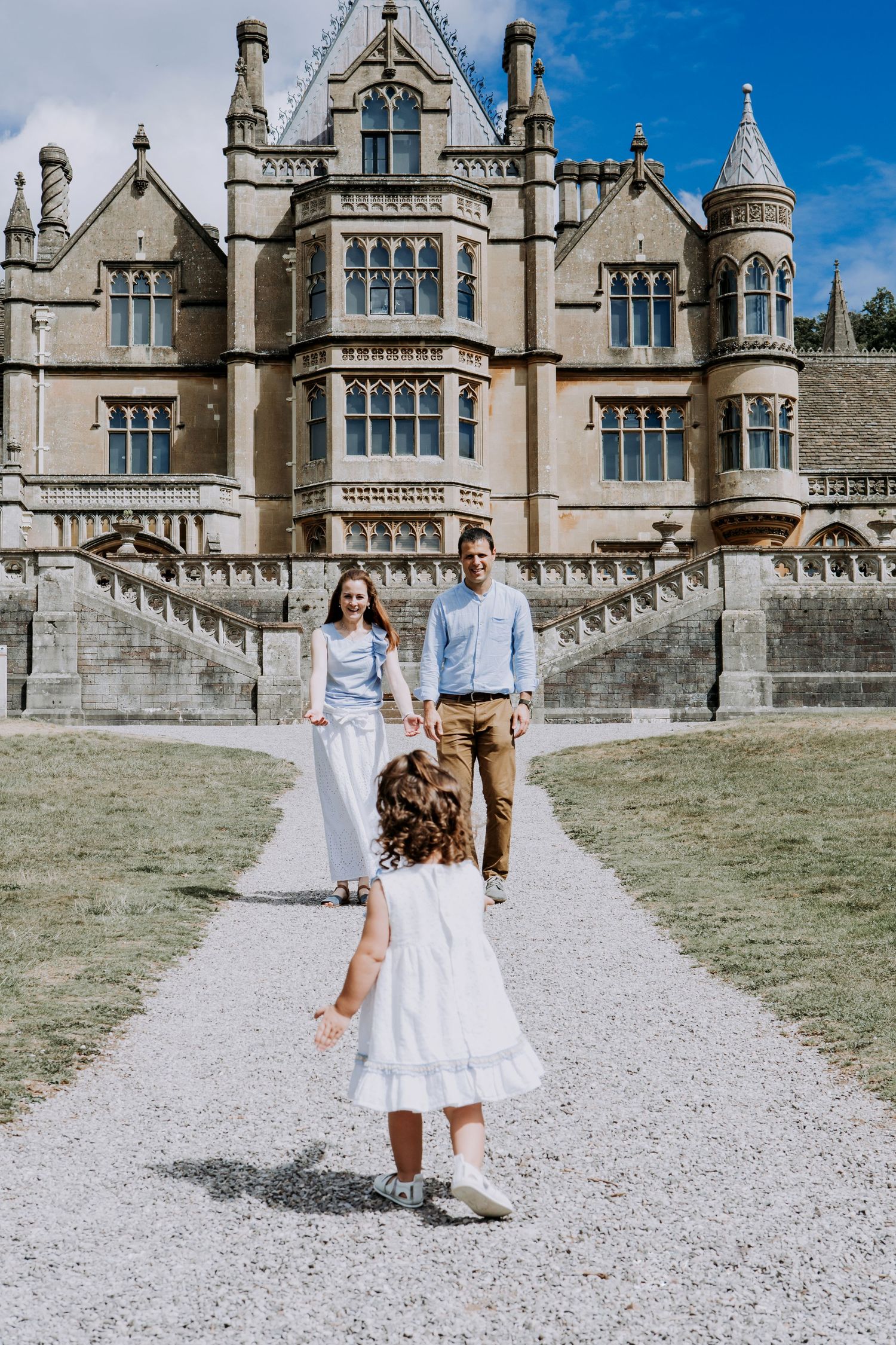 Parents walking towards their young daughter outside a historic country house during a family photography session in Somerset.