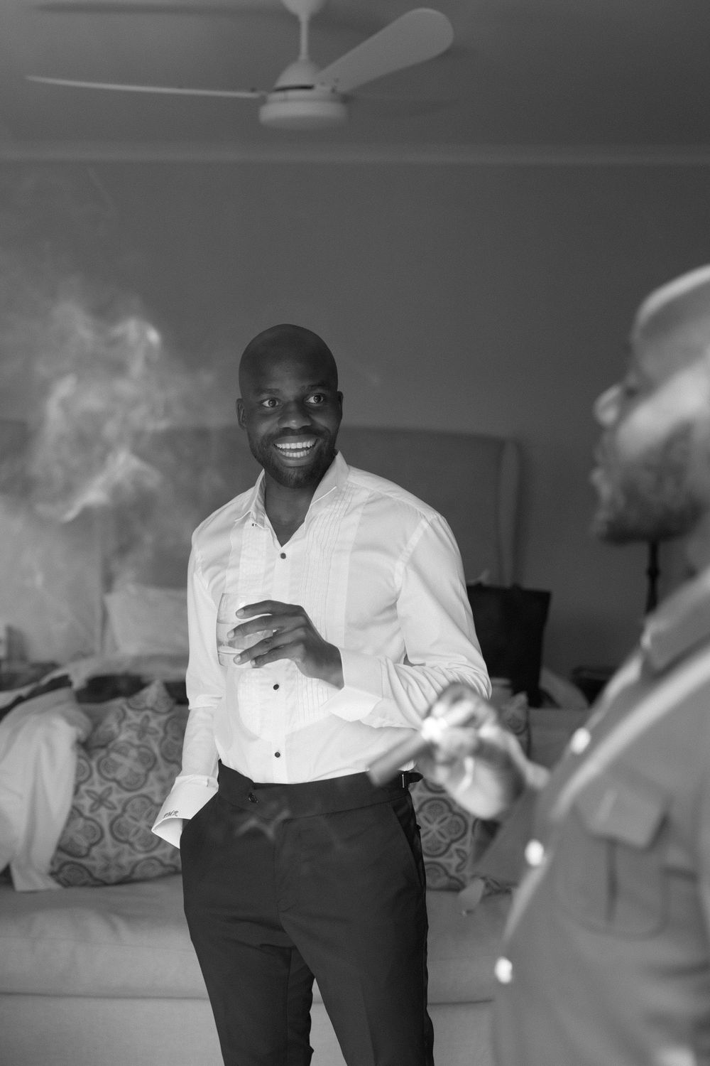 A smiling groom in a white dress shirt laughs with a groomsman in a black and white candid photo.