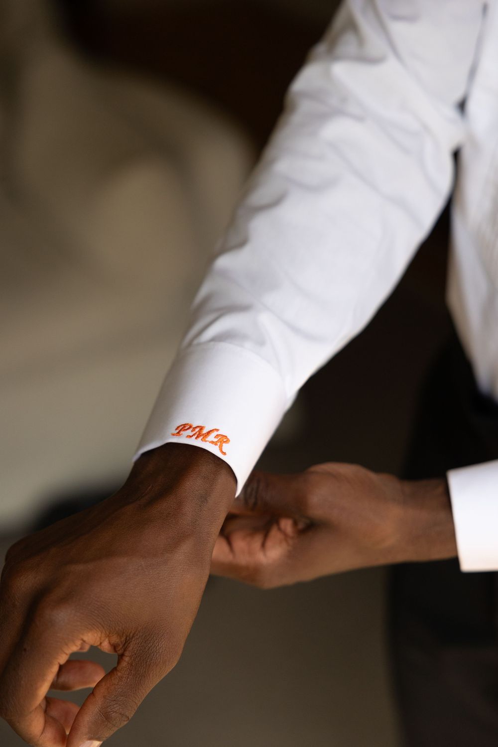 Close-up of a groom's white shirt cuff featuring orange embroidered monogram initials PMR.