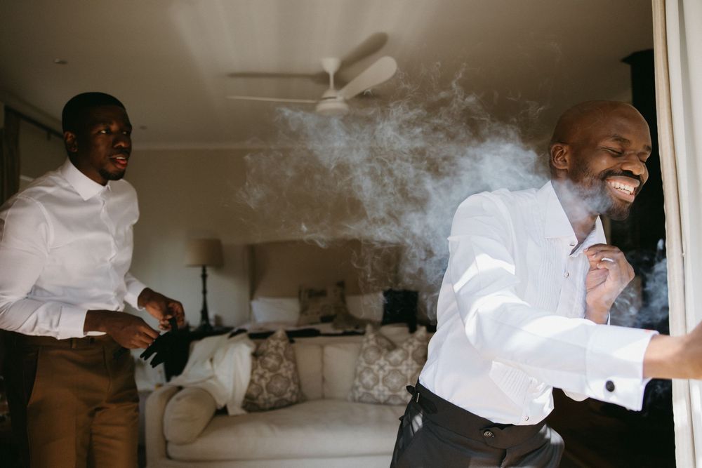 Two men in white shirts laughing and celebrating indoors, with smoke visible near one man's face.