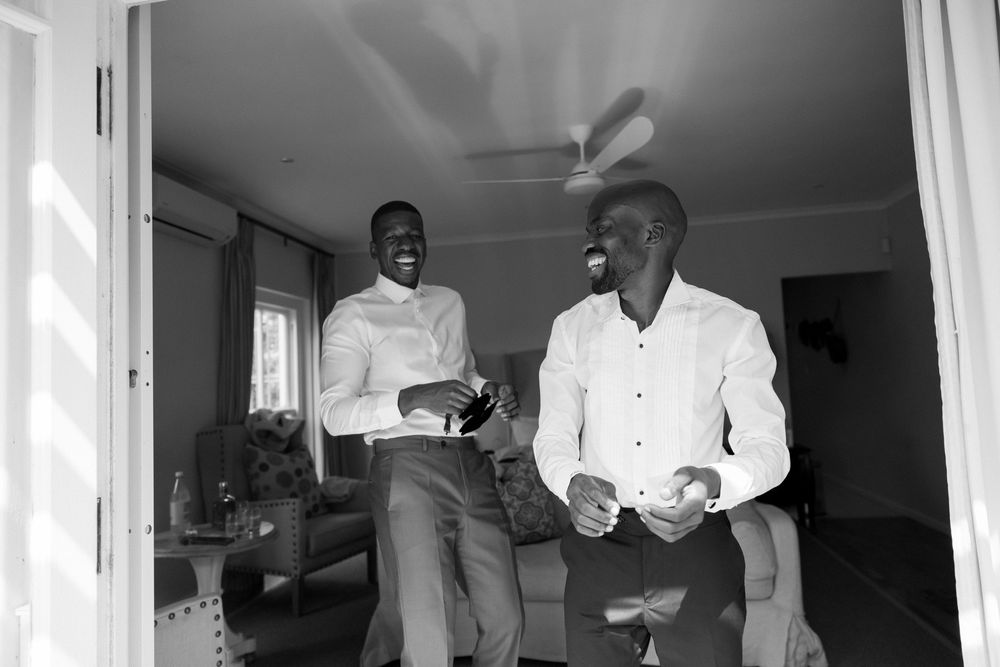 Two men in white shirts laughing together indoors in a black and white photo.