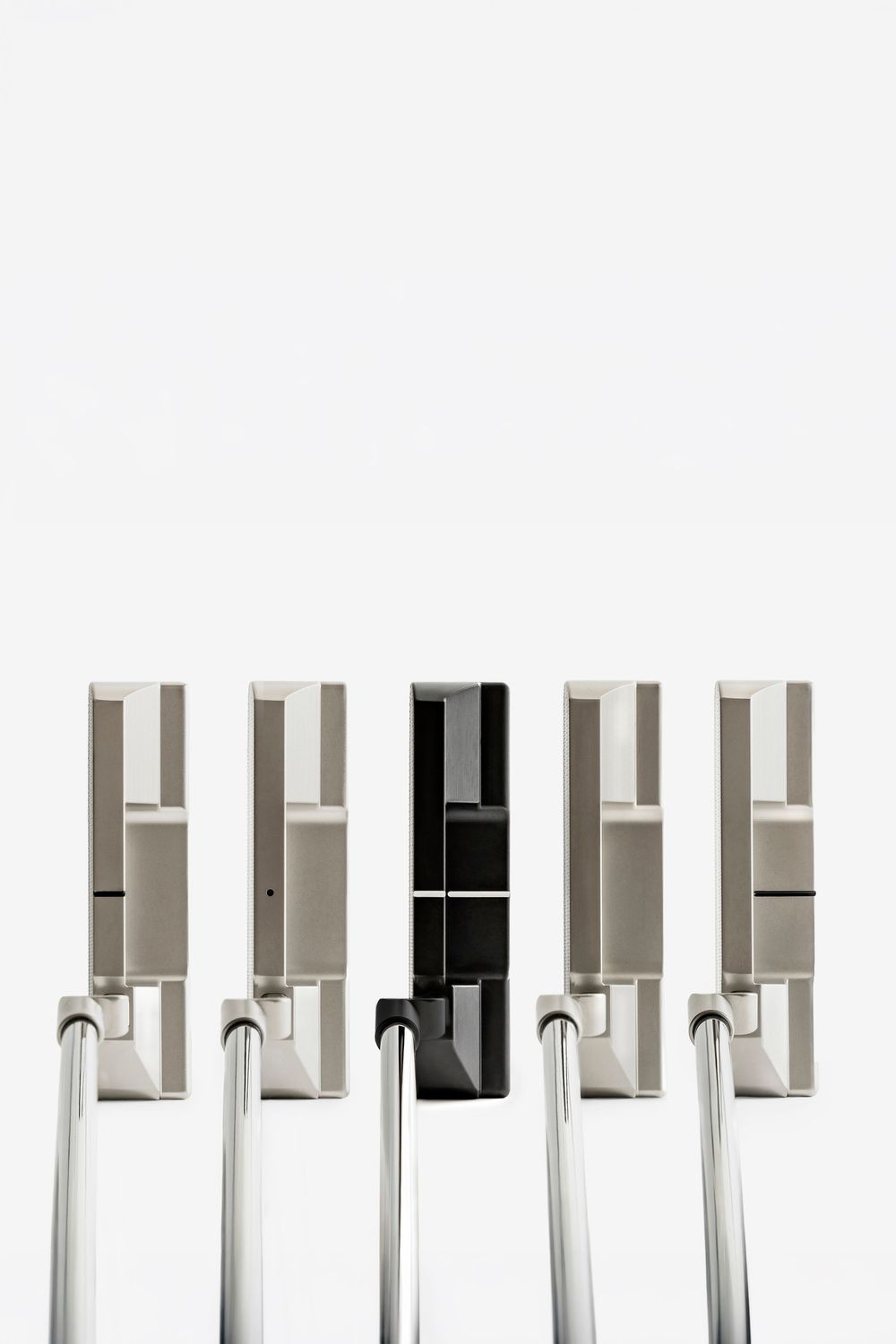 Five golf putters displayed side by side, with one black putter standing out among four silver putters against a white background.
