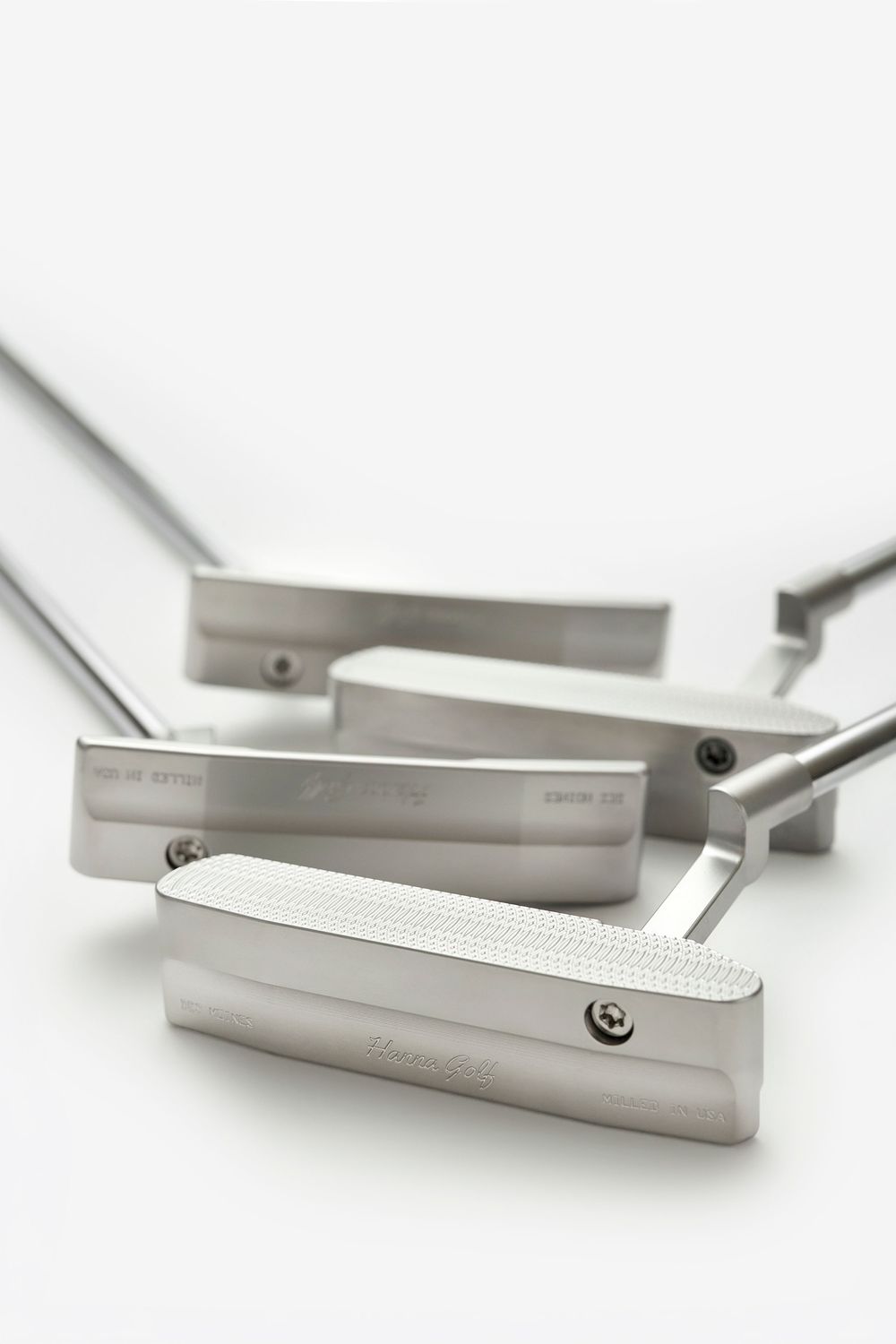 Three stainless steel golf putters arranged together, showcasing precision-milled blade heads with textured faces.