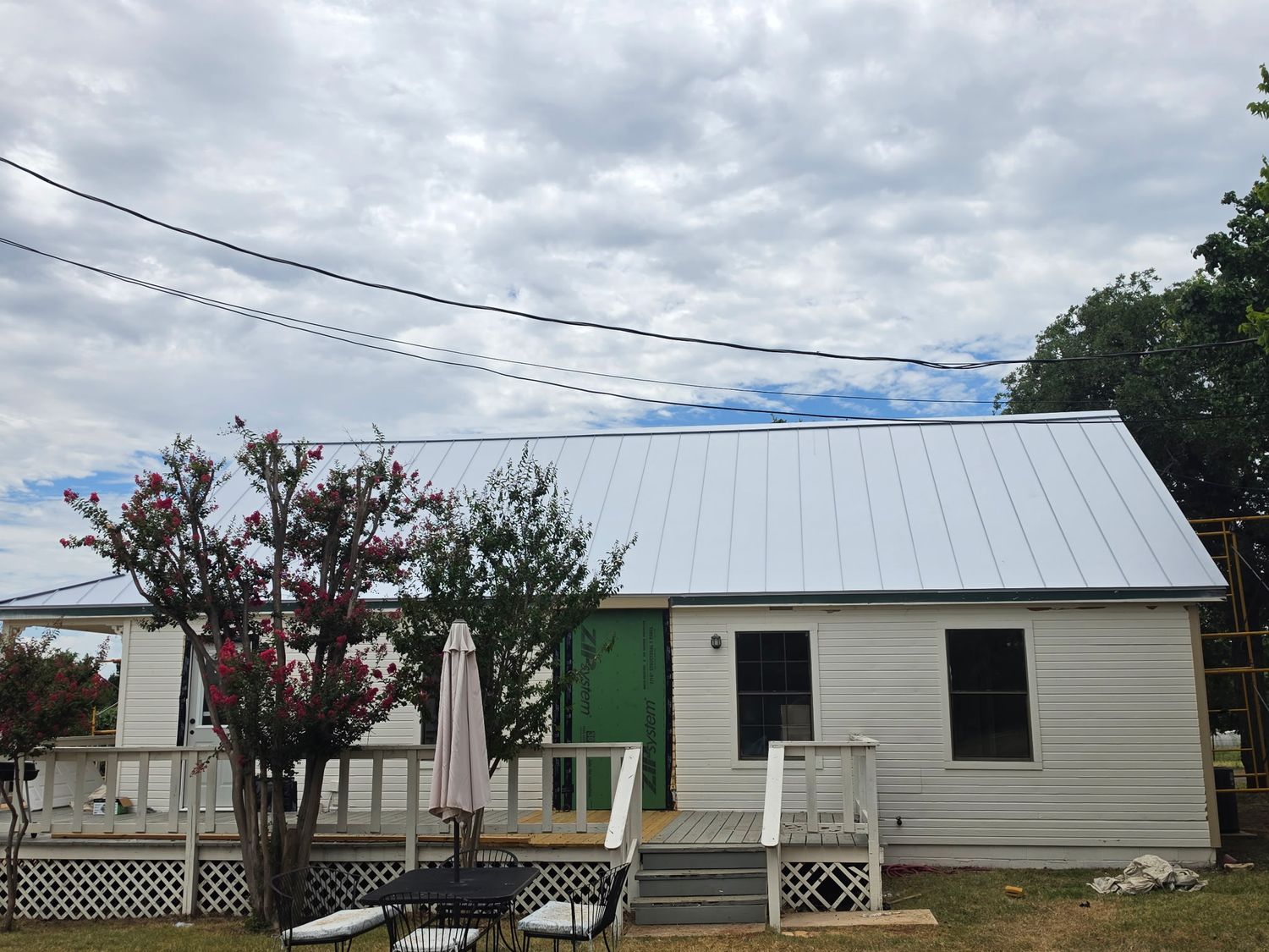 New metal standing seam roof installation on a white sided home with scaffolding visible beside the building.
