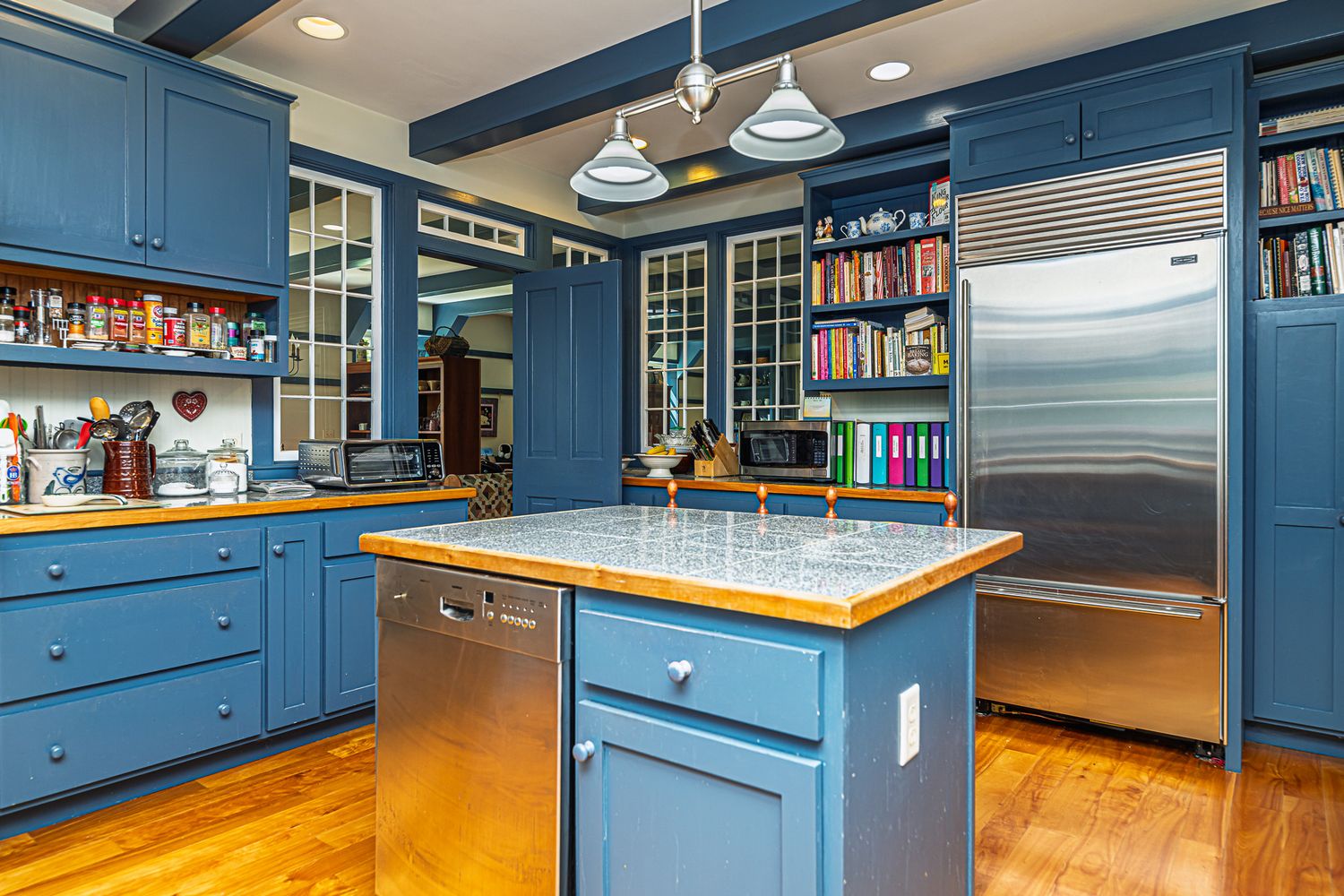 Modern kitchen with blue cabinetry, wood-top island, stainless steel fridge, and hardwood floors.