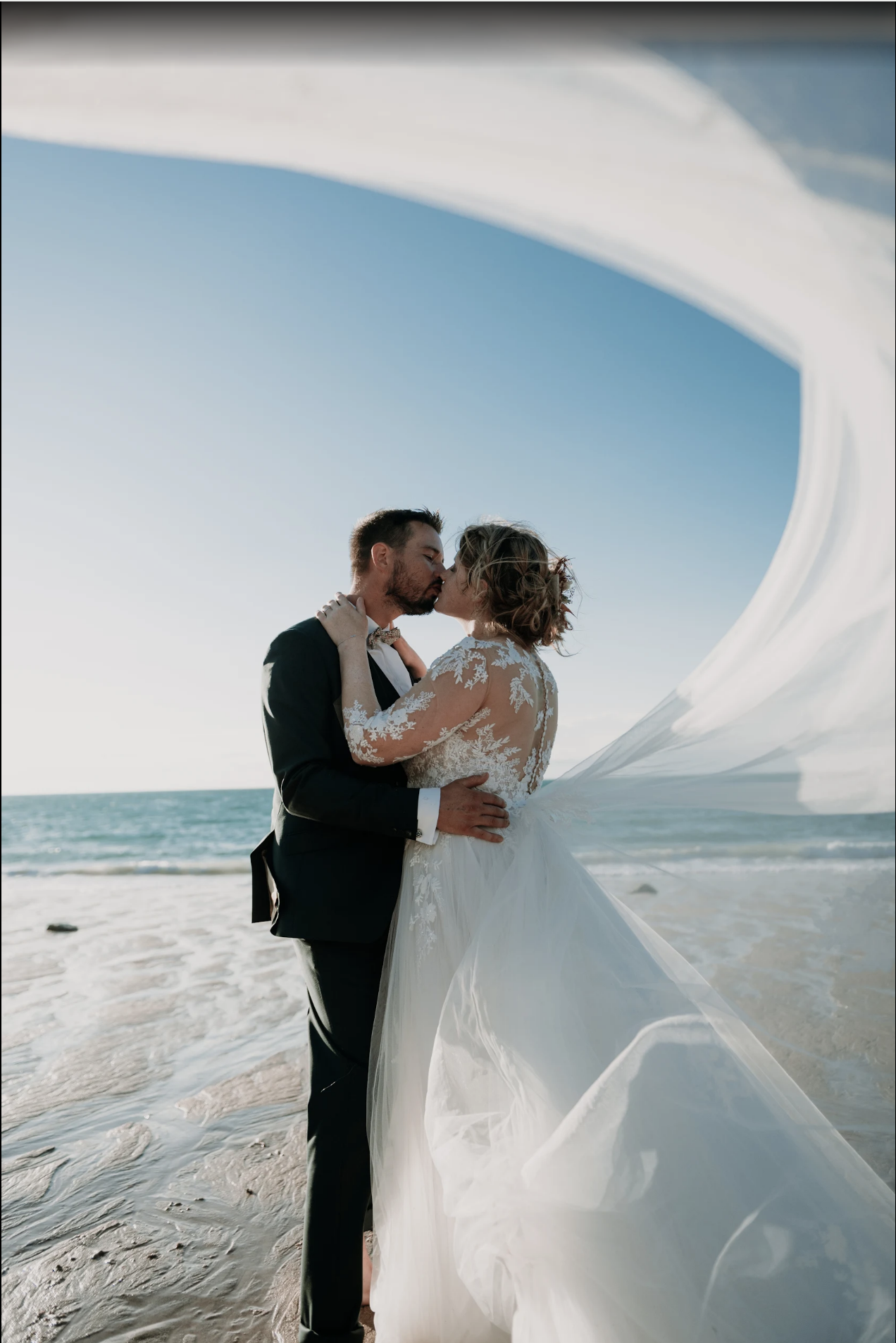 Couple de mariés enlacé face à la mer lors d’une séance photo de mariage