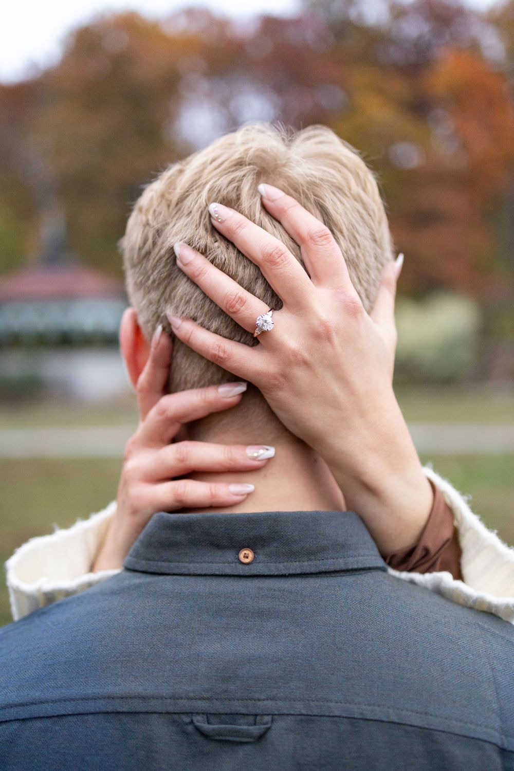 Woman with engagement ring resting hand on back of man's head outdoors in Eden Park during their Fall Engagement photoshoot in Cincinnati.