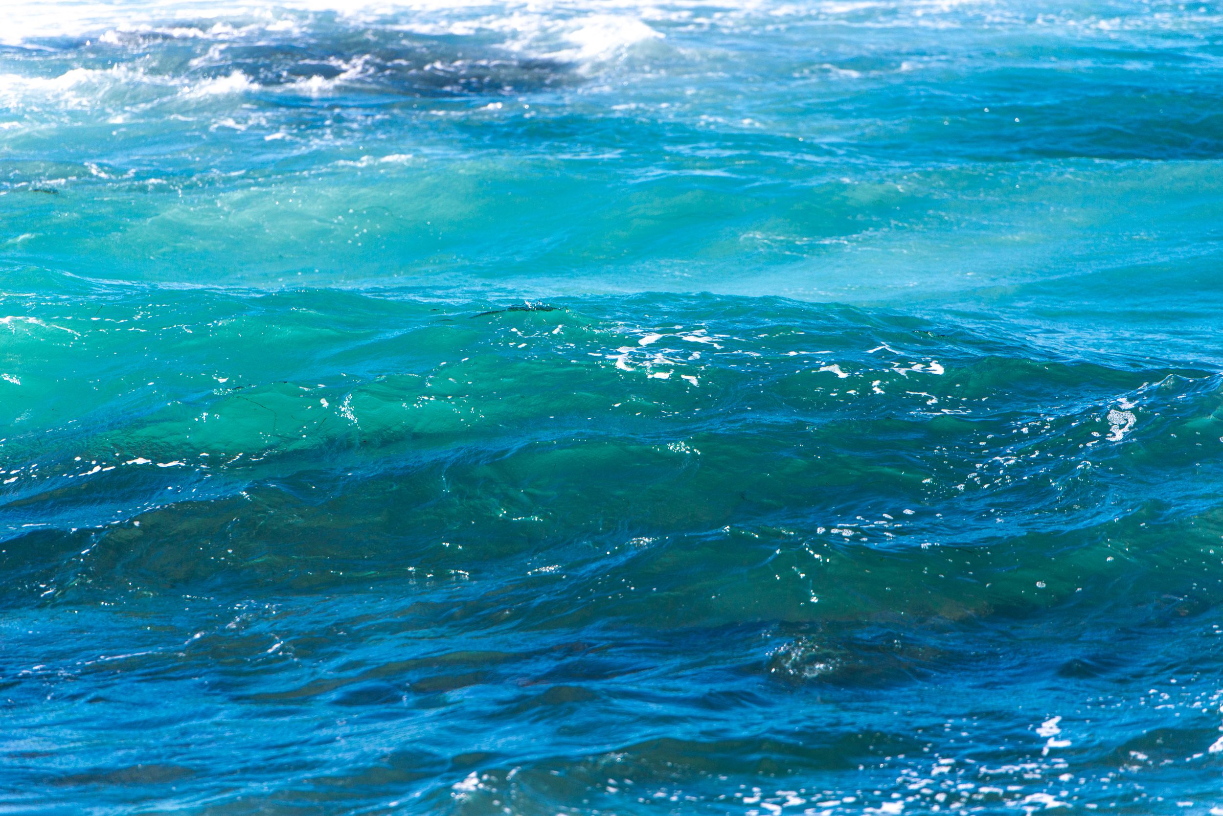 Vibrant turquoise and blue ocean waves with white sea foam, showcasing the stunning colors of clear tropical water.