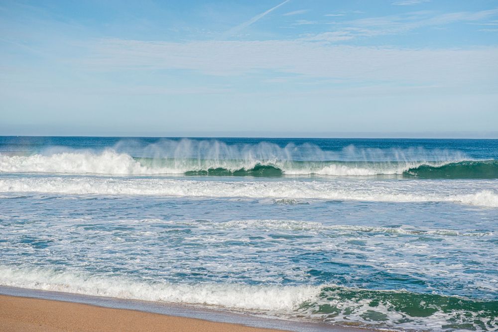 Powerful ocean waves crashing on a sandy beach under a clear blue sky on a sunny day.