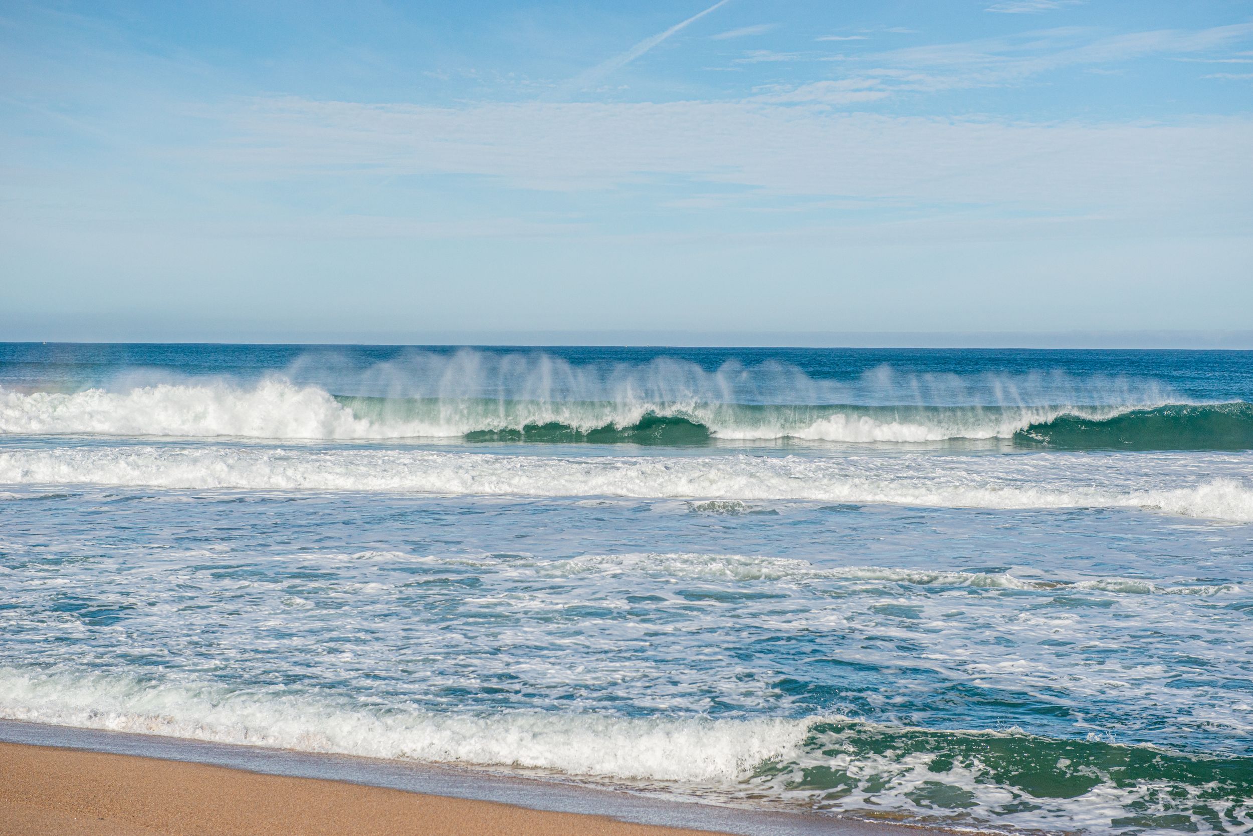 Powerful ocean waves crashing on a sandy beach under a clear blue sky on a sunny day.