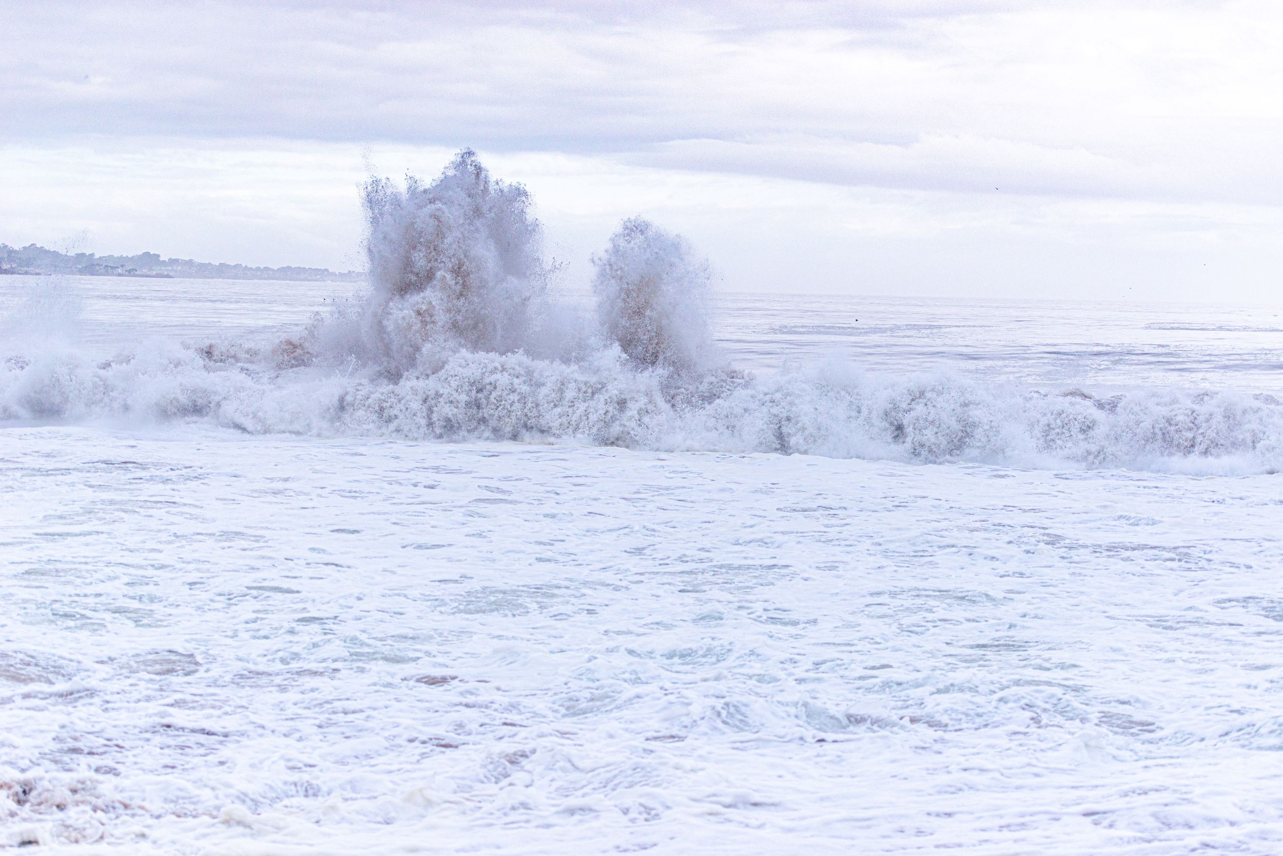 Frozen winter landscape with snow-covered waves and frost-encrusted vegetation under a pale overcast sky.