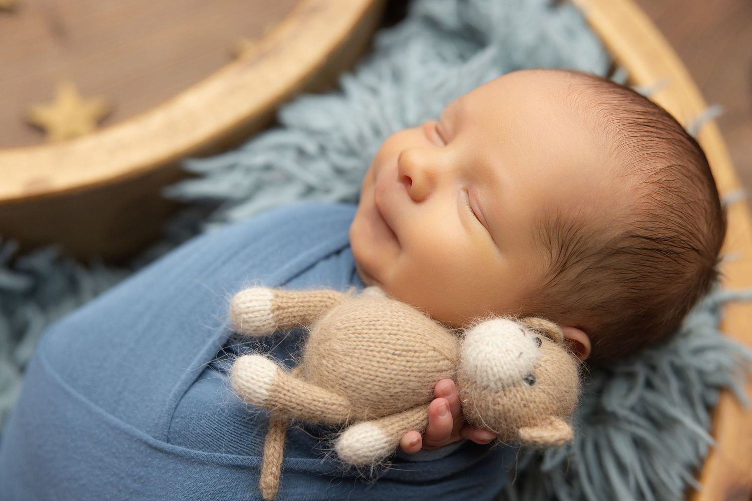 Newborn baby resting chin on hands inside a teal bucket with soft blanket, studio photography.