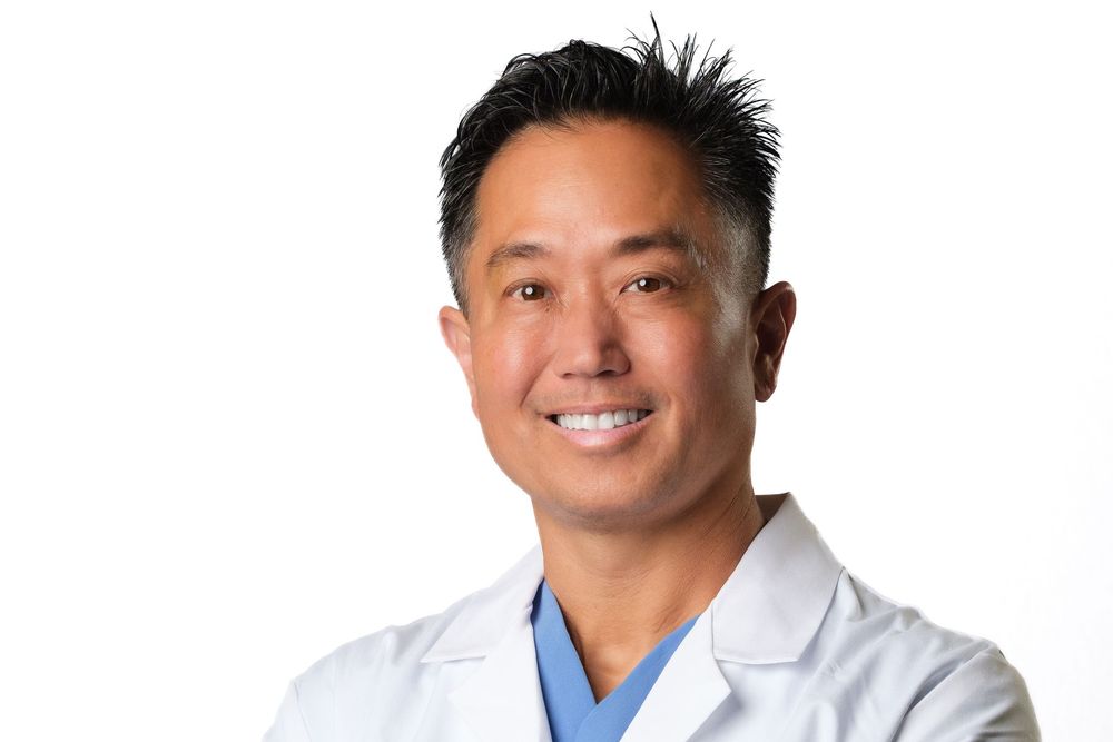 A smiling medical headshot of a doctor in a white lab coat against a white background.