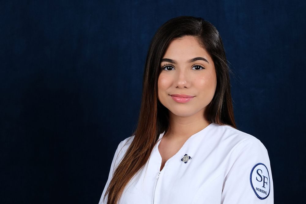 A headshot of a deaf nurse wearing white scrubs against a blue backdrop.